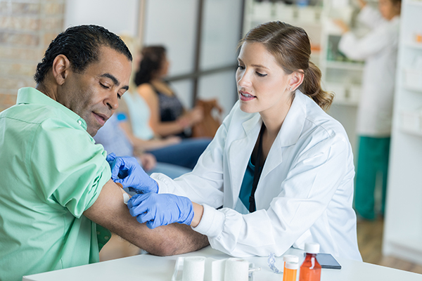 Doctora colocando curita en el brazo derecho de un paciente masculino