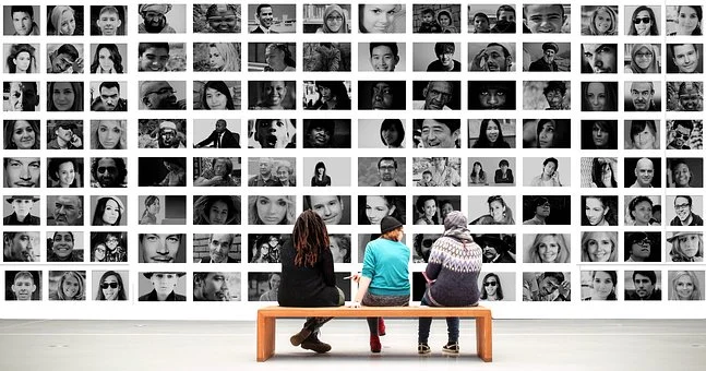 Teen sitting in from of a wall of photos of people.